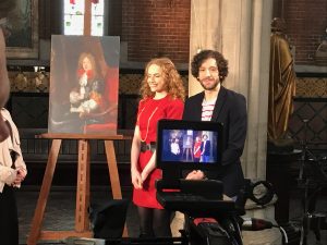 A behind the scenes photo of Greg Jenner and Professor Kate Williams filming Inside Versailles - Kate wears a red dress and Greg wears a striped t-shirt and navy jacket